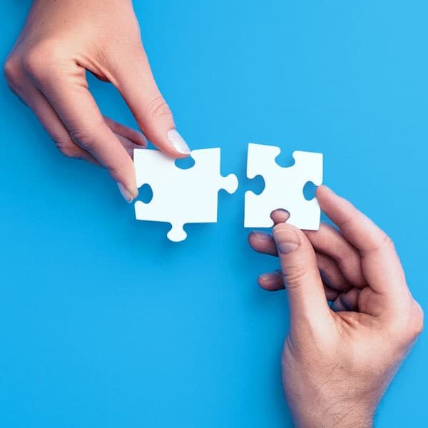 Two hands each holding interlocking puzzle pieces symbolize our devotion to collaboration.